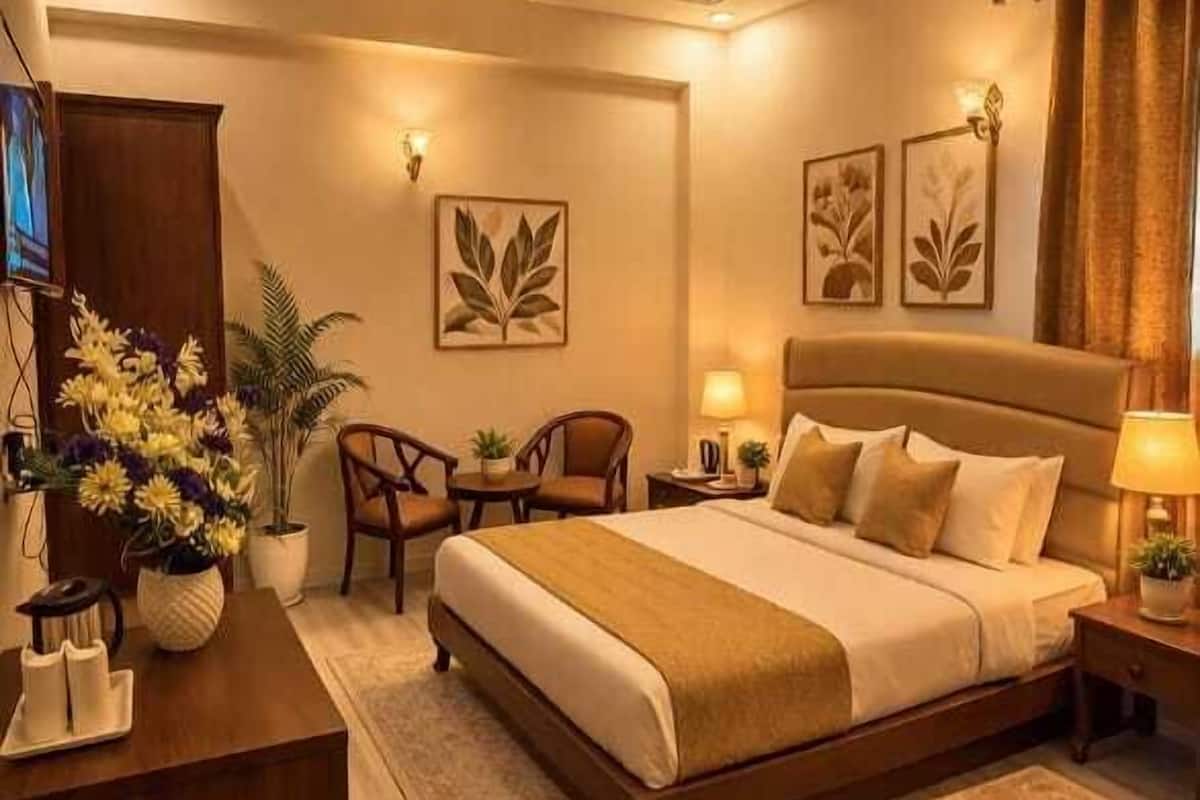 Una habitación de hotel con una cama grande, un escritorio, una silla, una mesita y una planta en maceta.