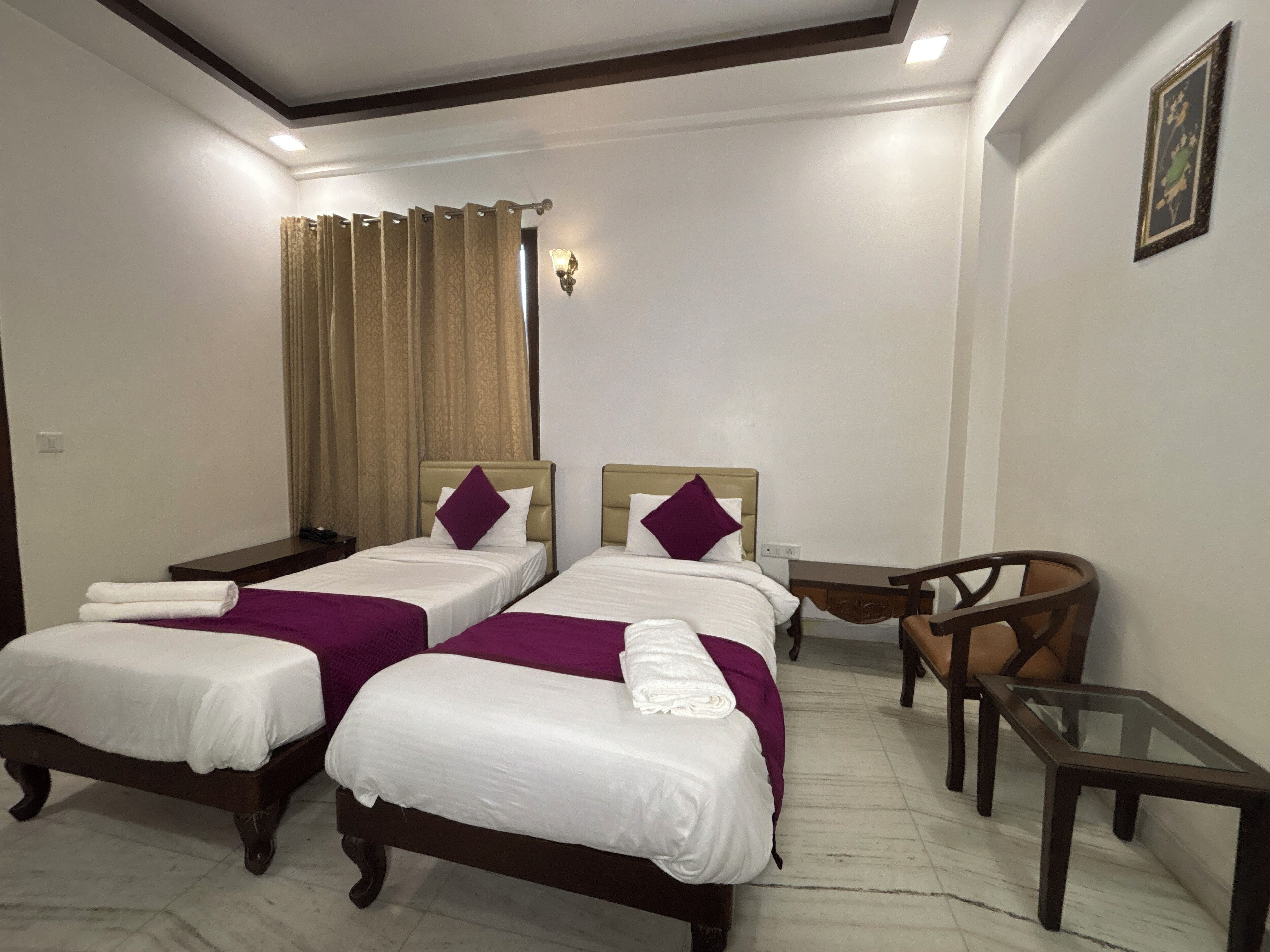 A hotel room with two beds, a chair, a small table, and a curtain.