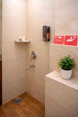 Zona de ducha con dispensador de toallas en la pared, una planta en maceta y un estante con artículos de aseo.