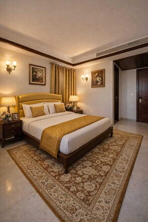 Habitación de hotel con una cama grande, dos mesitas de noche con lámparas, una alfombra estampada y cuadros en las paredes.