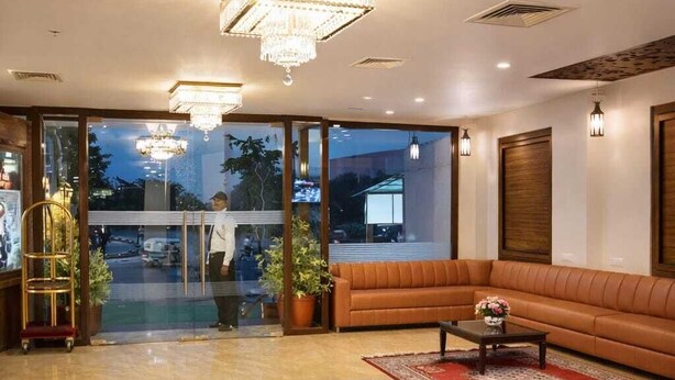 A spacious lobby with a large sofa, a coffee table, and a red rug. There are chandeliers and wall sconces providing lighting. - Goyal Hoteliers - Hotel The Agra Grande (Agra)