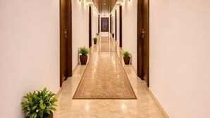 A hotel hallway with a wooden ceiling, marble floor, and wall-mounted lights. - Goyal Hoteliers - Hotel The Agra Grande (Agra)