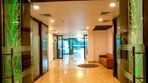 A hotel lobby with a polished marble floor, glass doors with green leaf patterns, and a sofa in the background. - Goyal Hoteliers - Hotel The Agra Grande (Agra)