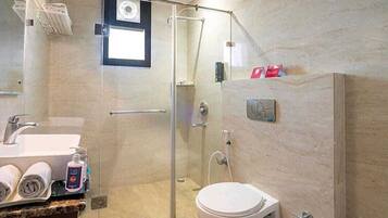 A modern bathroom with a glass shower enclosure, a toilet, and a sink with towels and toiletries.