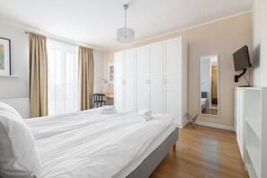 Una habitación de hotel con una cama grande, un armario blanco y un televisor en la pared.