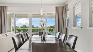 Un espace repas moderne avec une longue table, des sièges confortables et une vue sur une piscine et un jardin luxuriant.