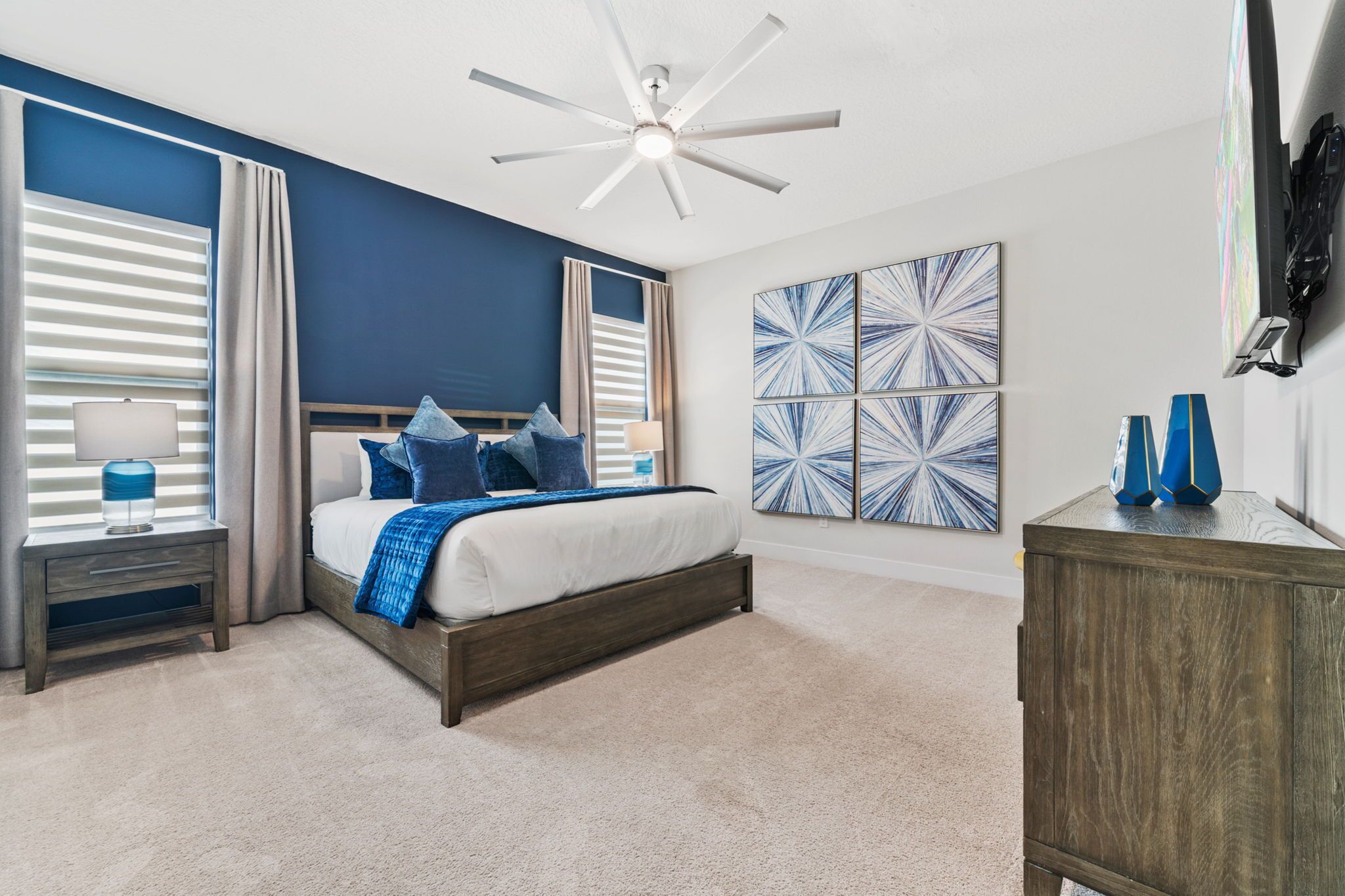 A bedroom with a bed, nightstands, a ceiling fan, and artwork on the walls.