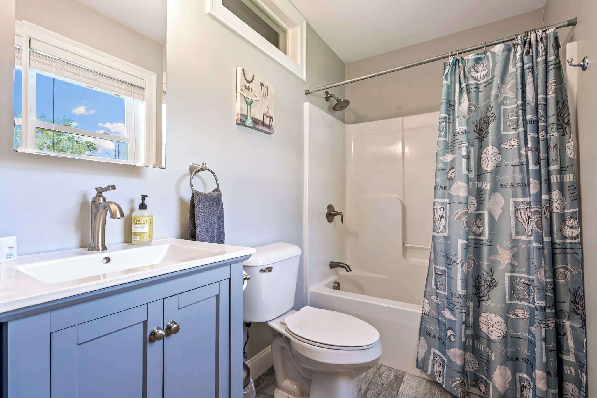 A bathroom with a white sink, a toilet, a bathtub, and a shower curtain with a sea-themed pattern.
