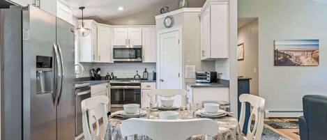 A modern kitchen with white cabinetry, stainless steel appliances, and a dining area with a table set for four.