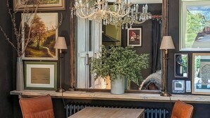 A room with a large mirror, a chandelier, framed artwork, a potted plant, and a wooden table.