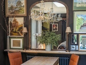 A room with a large mirror, a chandelier, framed artwork, a potted plant, and a wooden table.