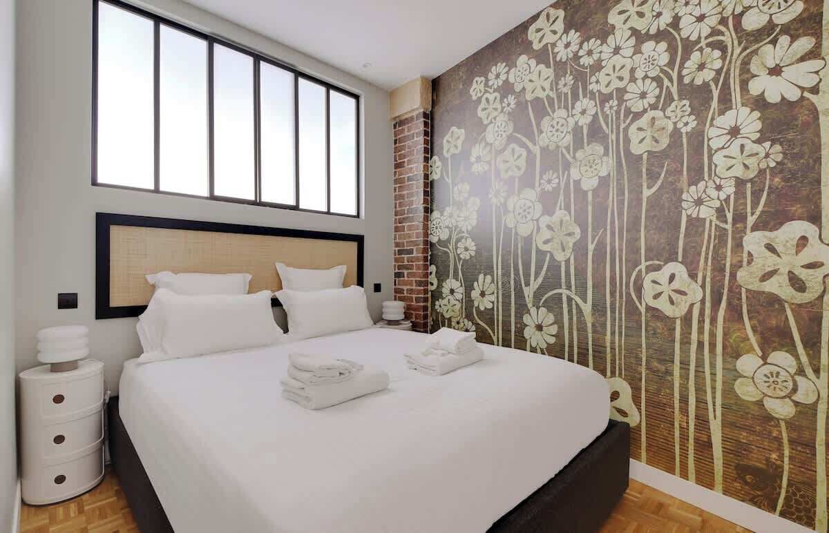 Une chambre d’hôtel avec un grand lit, un mur décoratif en briques et une fenêtre avec des stores.