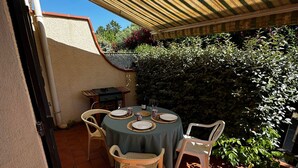 A patio with a round table set for four, surrounded by chairs, under a striped awning. - Charming pavilion in Argelès-sur-Mer - Beach 5 min, air conditioning, pets allowed (Argelès-sur-Mer)