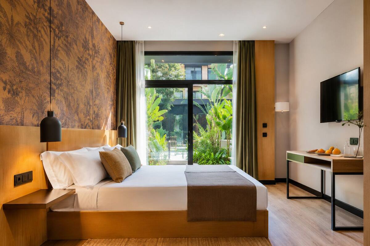 Una habitación de hotel moderna con cama, mesita de noche, televisor y vistas al exterior.