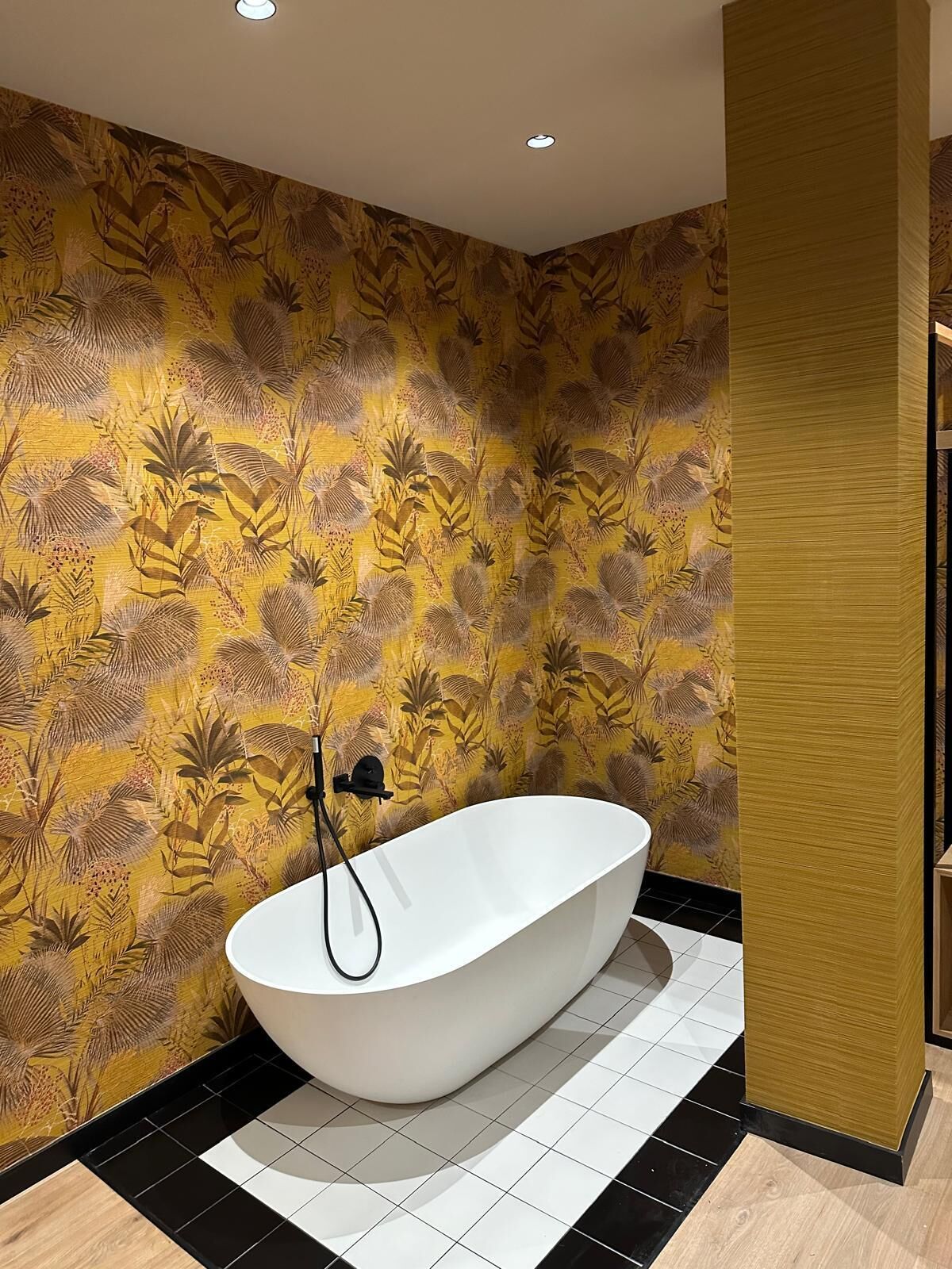 A modern bathroom with a freestanding bathtub, patterned wallpaper, and a wooden accent wall.