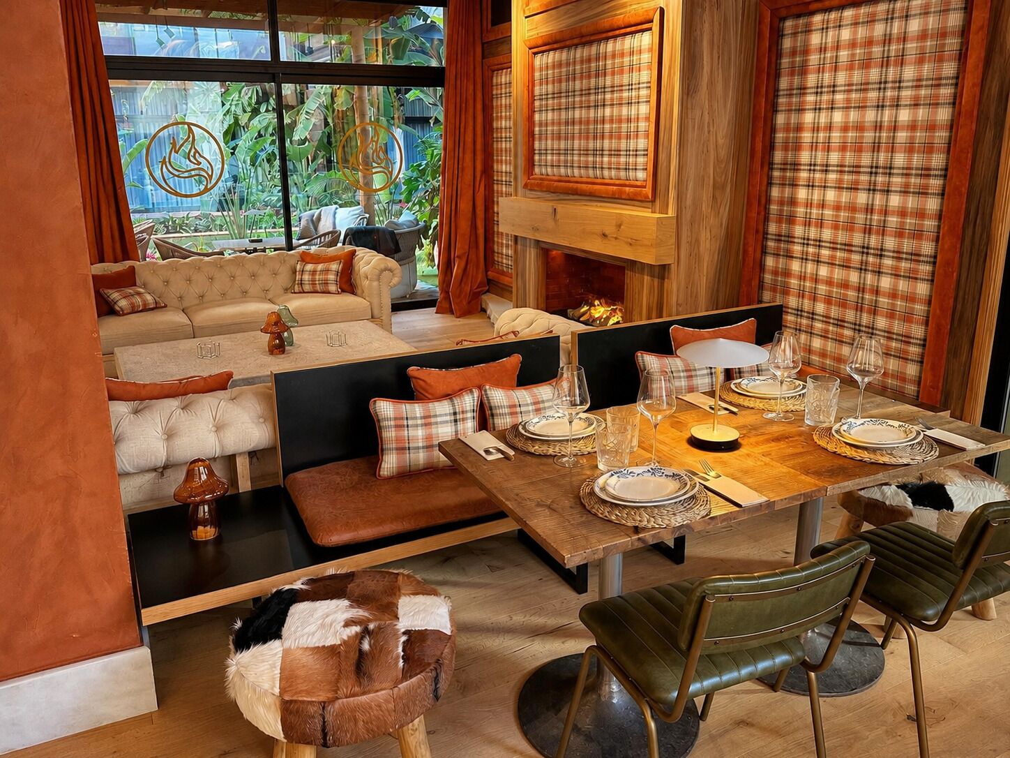 A cozy dining area with a wooden table set for four, surrounded by plush seating and a view of greenery outside.