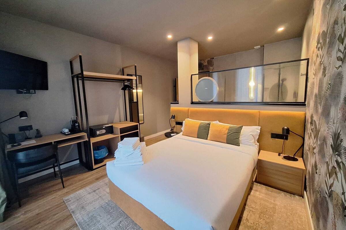 Una habitación de hotel moderna con una cama grande, mesitas de noche, un escritorio con silla, un televisor y un espejo.