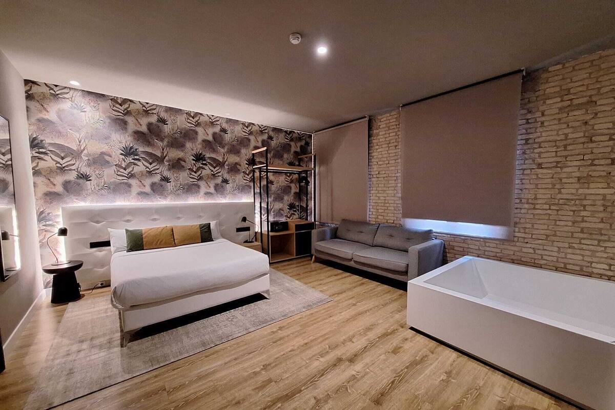 Un dormitorio moderno con una cama grande, un sofá, una bañera blanca y una pared de ladrillo.