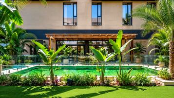 Un edificio moderno con piscina, rodeado de exuberante vegetación y una pérgola.
