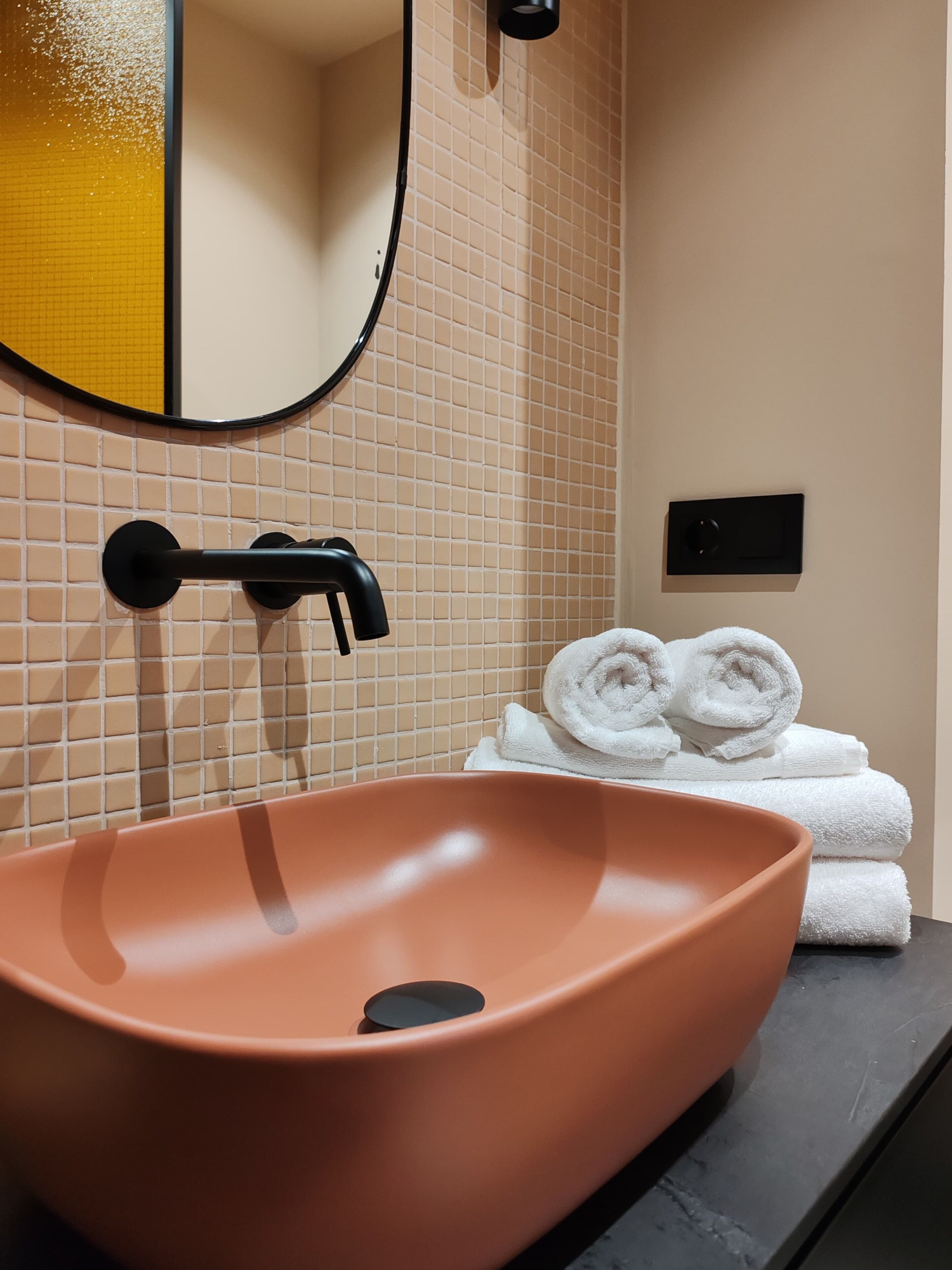 A bathroom with a large oval sink, a mirror, and a towel rack with folded towels.