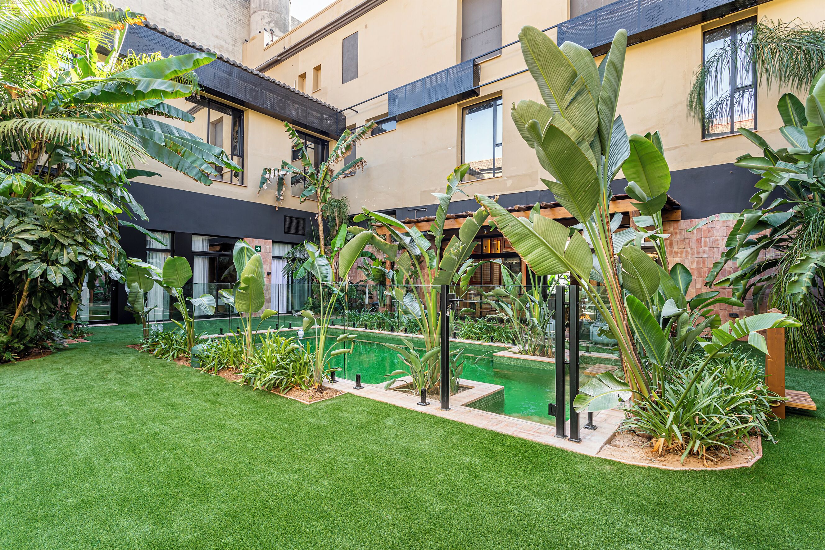 A courtyard with a swimming pool, lush greenery, and a modern building facade.