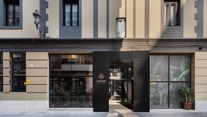 A modern hotel entrance with a glass facade, a prominent logo, and a potted plant outside. - Saman Boutique Hotel (Valencia)