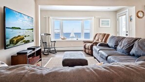 A living room with a large window, a sofa, a television, and a rocking chair. - Wright by the Sea For 10! (York Beach)