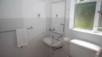 A bathroom with a white sink, mirror, and toilet, with a towel rack and a window with frosted glass.