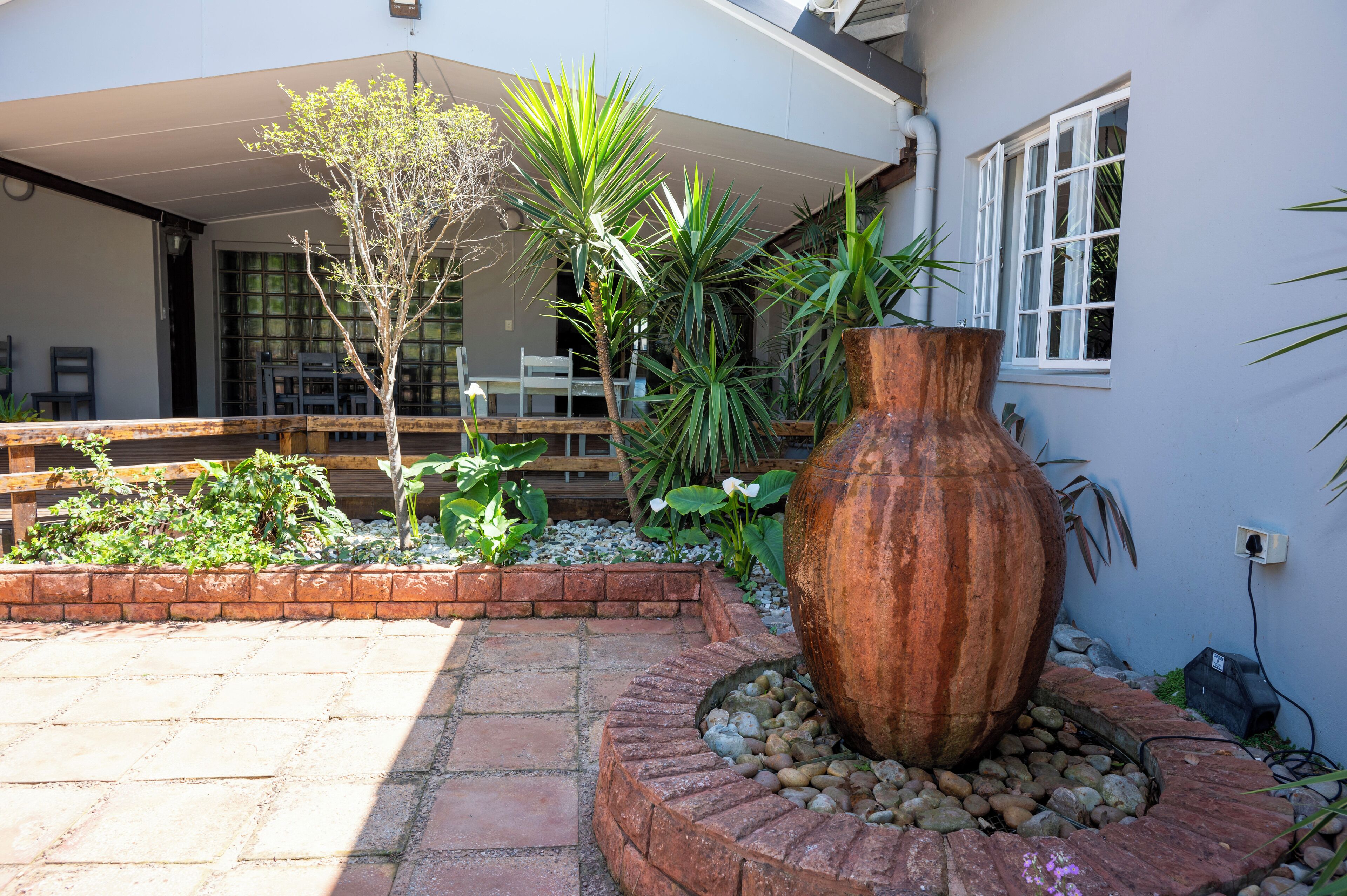 Un patio con una jardinera grande, un banco de madera y una mesa bajo una sección cubierta.