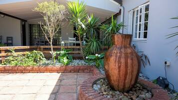 Un patio con una jardinera grande, un banco de madera y una mesa bajo una sección cubierta.