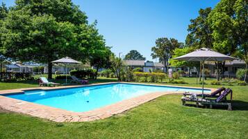 Una piscina al aire libre, sombrillas, sillones reclinables de piscina