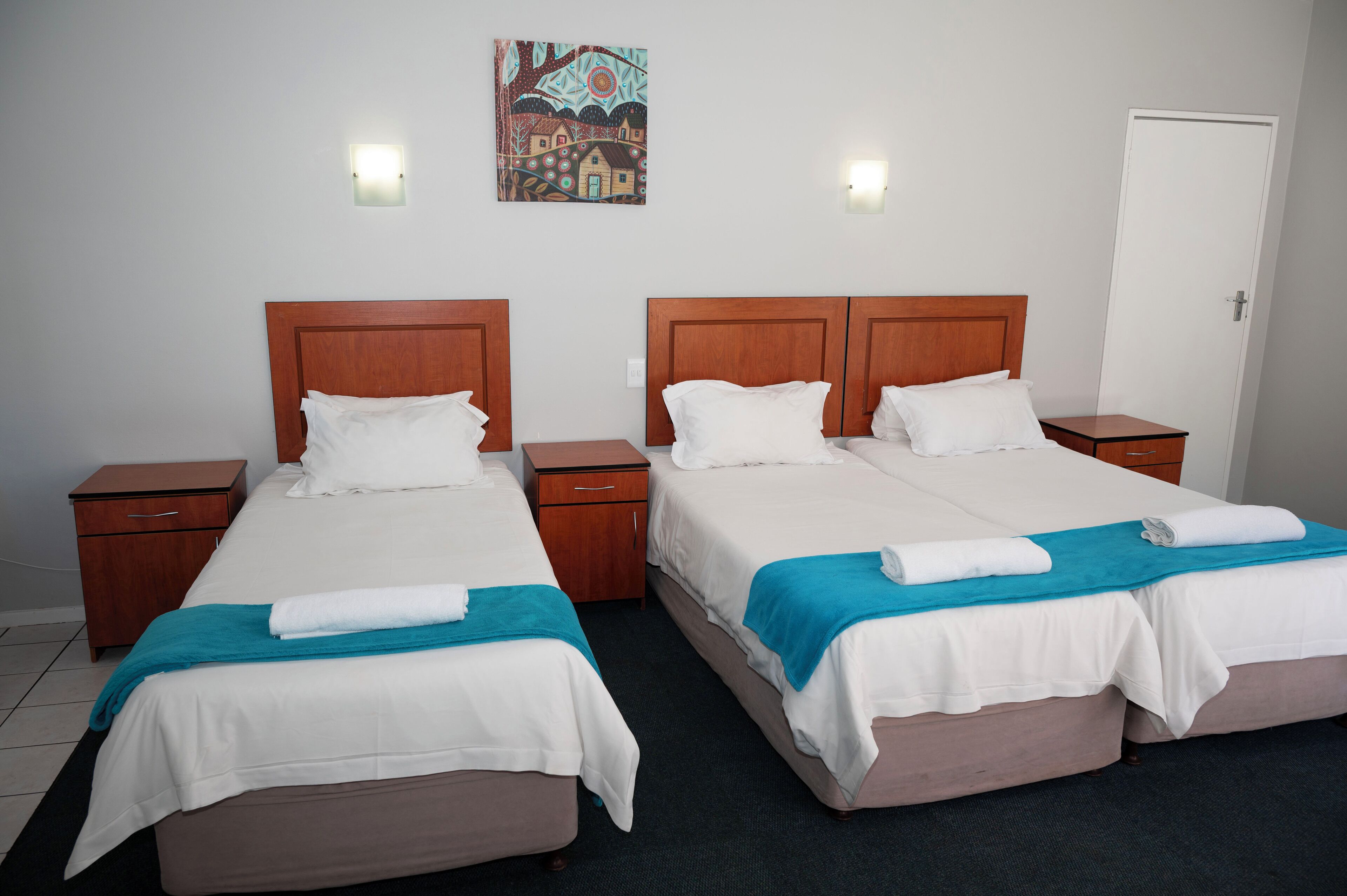 A hotel room with two beds, wooden headboards, white bedding, and a teal throw blanket.