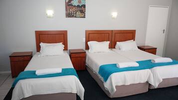 A hotel room with two beds, wooden headboards, white bedding, and a teal throw blanket.
