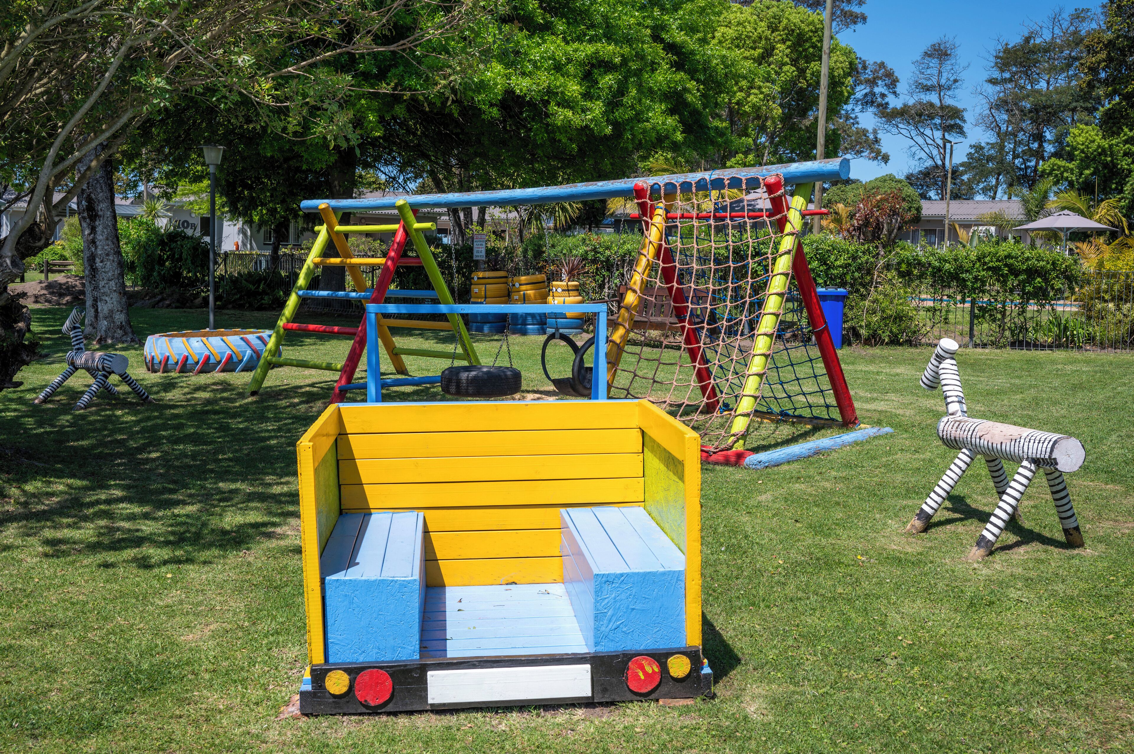 Une aire de jeux avec un toboggan jaune et bleu, une structure d’escalade et un espace de jeu délimité par un filet.