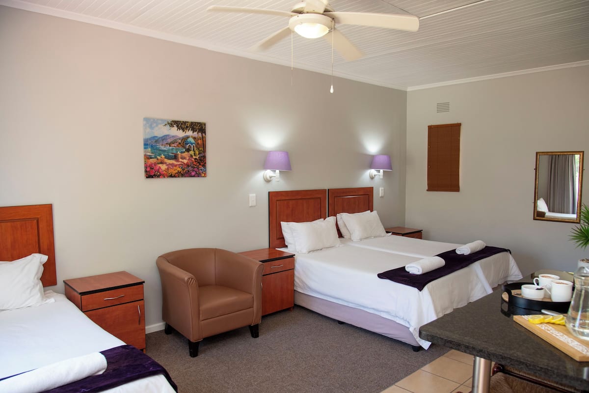 A hotel room with two beds, a chair, a desk with a coffee setup, and a ceiling fan.