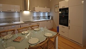 A modern kitchen with white cabinets, a built-in oven, and a dining table set for four.