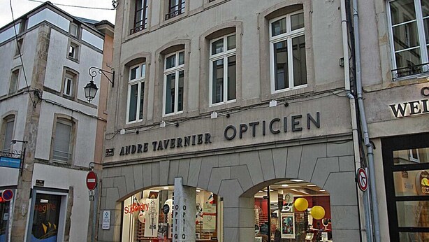 A building with a sign reading "ANDRE TAVERNIER OPTICIEN" and a storefront with various items on display.