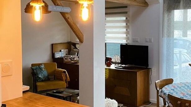 A cozy living room with a wooden table, a yellow armchair, and a television.