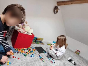 A child playing with building blocks on a carpeted floor, with a red storage box and a wall-mounted light fixture in the background.