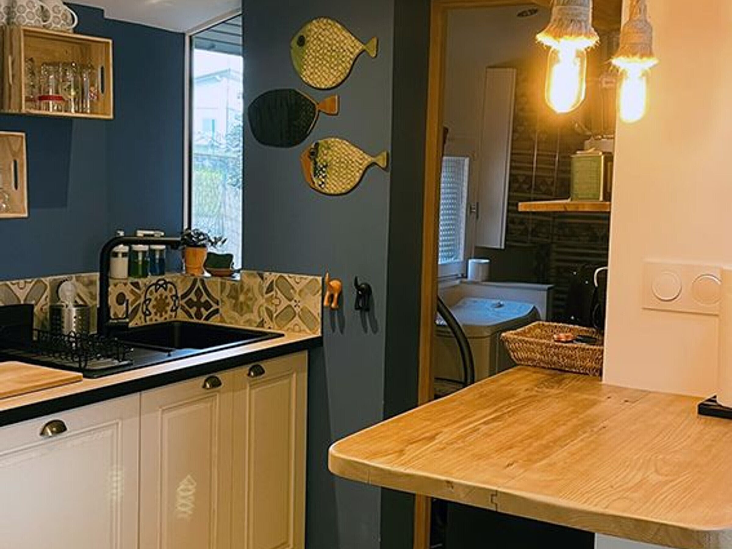 A kitchen with a black stove, white cabinets, and a wooden countertop. There are fish-shaped wall decorations and a window with blinds.