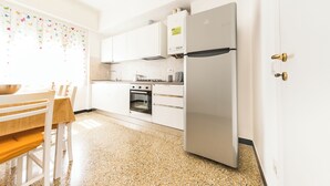 Une cuisine moderne avec des meubles blancs, un réfrigérateur en acier inoxydable, un four et un coin repas comprenant une table et des chaises en bois.