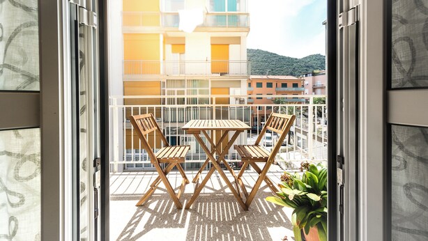 Un balcon avec une table et des chaises en bois, donnant sur un immeuble doté de balcons, avec une montagne en arrière-plan.