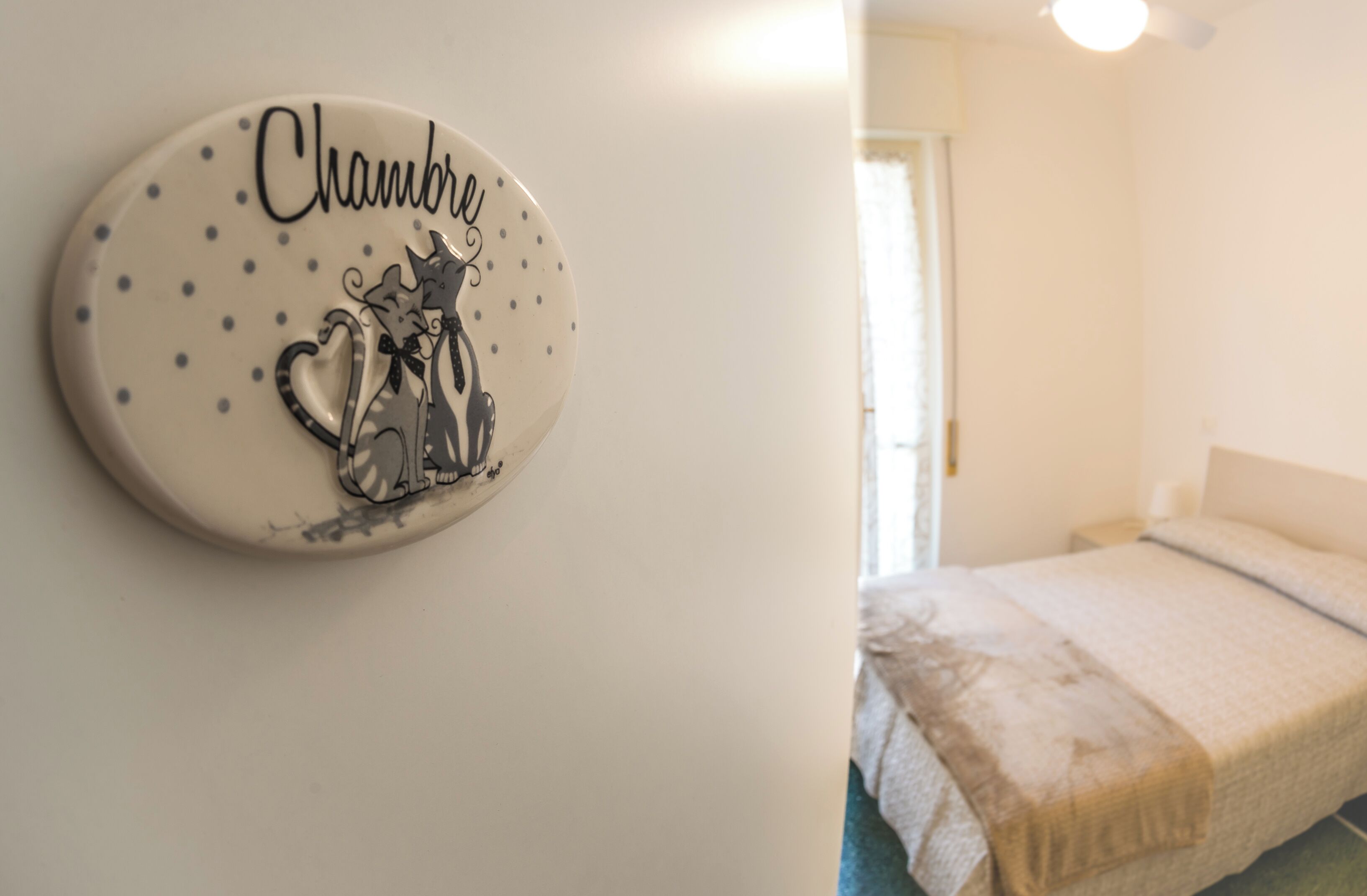 Une chambre à coucher avec un lit, un élément décoratif fixé au mur portant le nom « Chambro », et une porte donnant sur une autre pièce.
