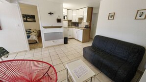 Een knus verblijf met een kitchenette, een bank, een rode stoel en een kleine tafel met papieren.