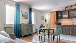 A cozy living room with a sofa, a dining table with chairs, a kitchen area with cabinets and a microwave, and a window with curtains.