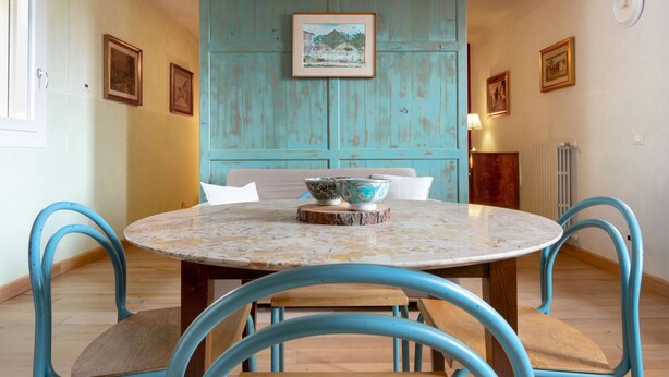 A dining area with a round table, four chairs, a wooden cabinet, and a wall with framed pictures.