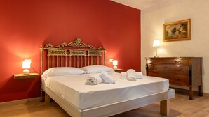A neatly made bed with white linens and towels, a wooden headboard, a bedside table with a lamp, and a wooden dresser with drawers.