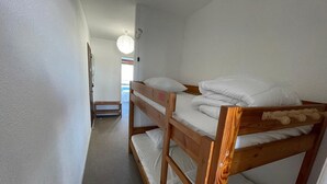 Een slaapkamer met een stapelbed, witte beddengoed, een houten hoofdbord en een klein houten krukje.