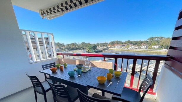Een balkon met een tafel gedekt voor vier personen, stoelen en uitzicht op een jachthaven en gebouwen.