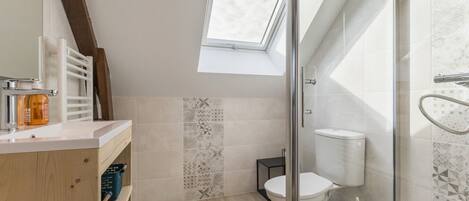 Et moderne badeværelse med ovenlys, glasvæg omkring brusebad og toilet.
